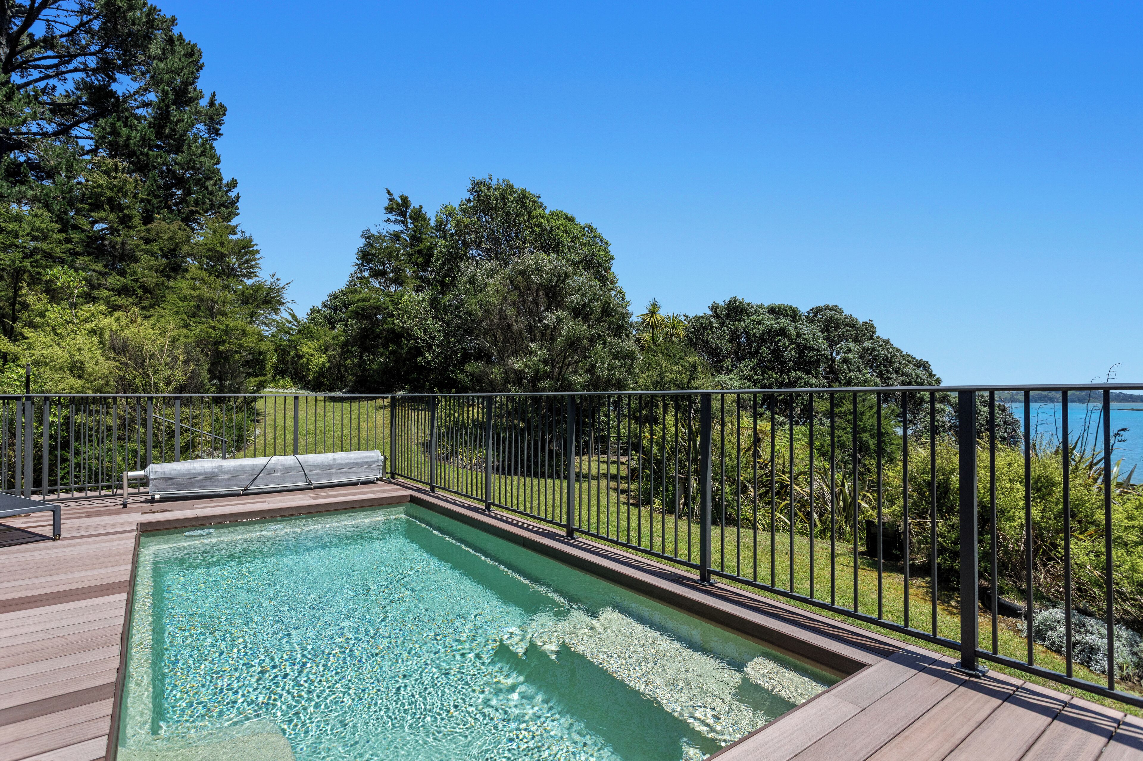 A rectangular swimming pool with clear water, surrounded by a wooden deck and a metal fence.
