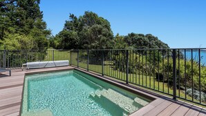 Une piscine rectangulaire à l’eau claire, entourée d’une terrasse en bois et d’une clôture en métal.