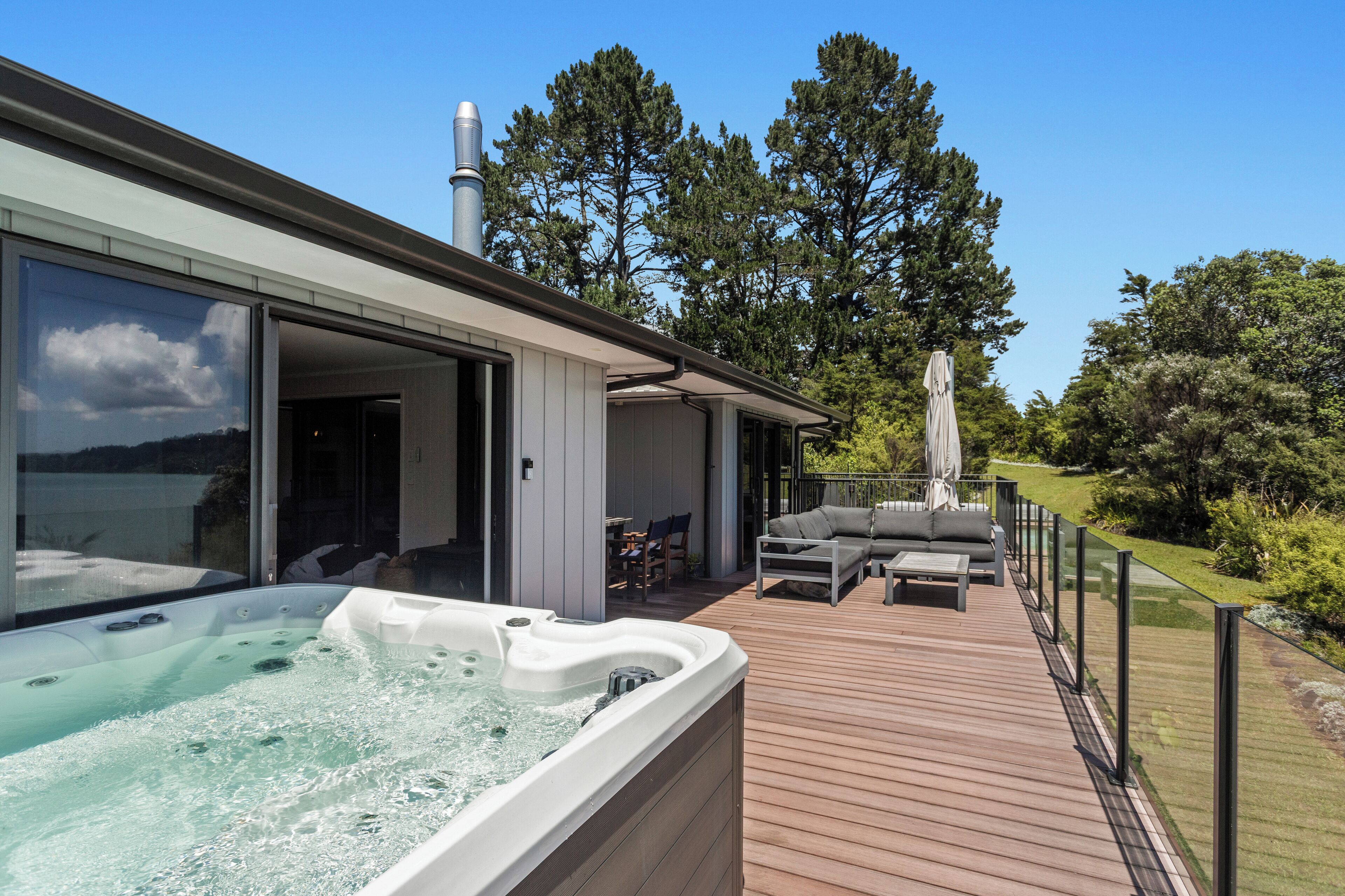 A modern outdoor deck with a hot tub, outdoor seating, and a view of the surrounding nature.