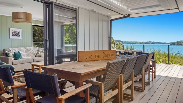 Une terrasse en bois avec une table et des chaises, une pancarte sur laquelle on peut lire « Vivre le rêve », et une vue sur un lac.