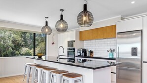 Une cuisine moderne dotée d’un îlot central, d’appareils électroménagers en acier inoxydable et de luminaires suspendus.