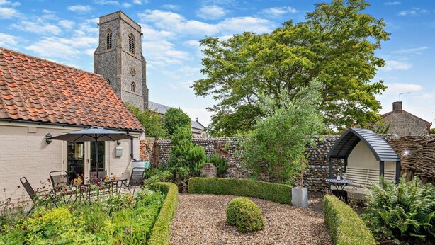 A courtyard with a stone wall, a small garden, and a building with a tiled roof. - 3 Bed in Trunch (oc-t29507) (Trunch)