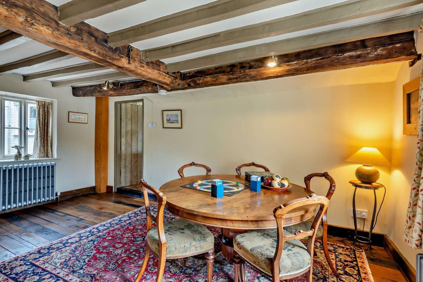 Un comedor con una mesa y sillas de madera, un tapete estampado y una lámpara.