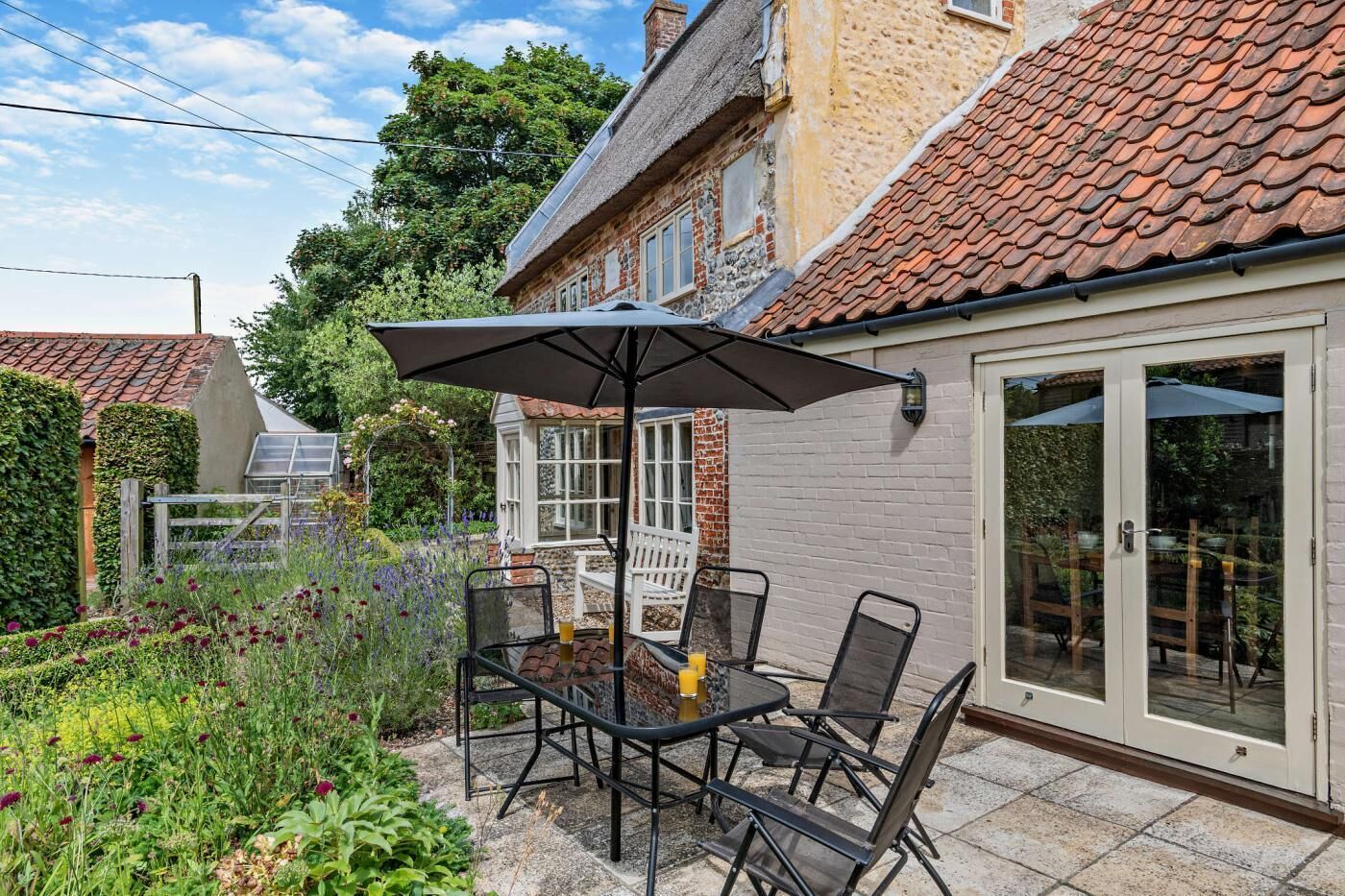 Una veranda con tavolo e sedie, una porta in vetro e un giardino con diverse piante.