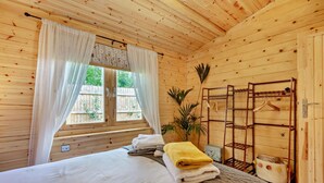 Quarto de cabana de madeira com cama, um varal e uma janela com cortinas.