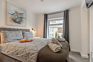 Ein Hotelzimmer mit einem Bett, einem Gemälde, einem Fenster mit Vorhängen und einem Frühstückswagen.