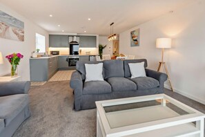 Ein modernes Wohnzimmer mit grauem Sofa, einem Couchtisch und einer Küche im Hintergrund.