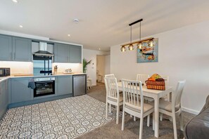 Eine moderne Küche mit grauen Schränken, einem eingebauten Backofen und einem Essbereich mit weißem Tisch und Stühlen.