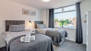 Quarto com duas camas, mesa de cabeceira, abajur, janela com cortinas e vista para a cidade.