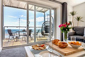 Une chambre avec un balcon donnant sur la mer, comprenant une table à manger avec de la nourriture, un canapé et un vase de fleurs.