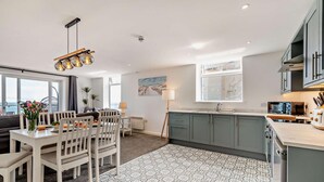 A modern kitchen with grey cabinets, a dining area with white chairs, and a patterned rug.