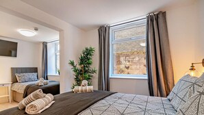 Ein modernes Hotelzimmer mit einem großen Bett, einem kleineren Bett, einem Schreibtisch und einem Fenster mit Vorhängen.