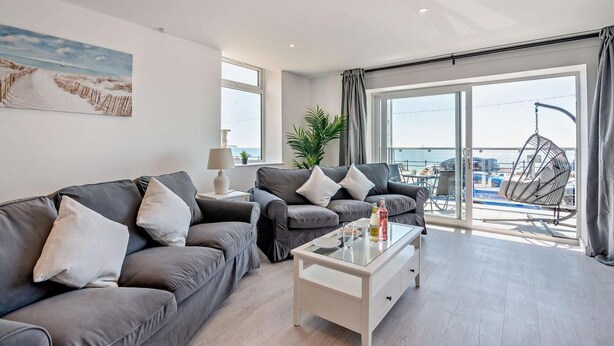 Ein modernes Wohnzimmer mit zwei grauen Sofas, einem Glastisch und Meerblick durch große Fenster.