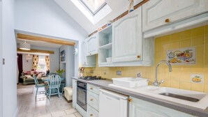 Et køkken med hvide skabe, en gul backsplash, en vask og et spiseområde med et bord og stole.
