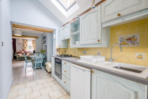 A kitchen with white cabinets, a yellow backsplash, a sink, and a dining area with a table and chairs. - 2 Bed in Heacham (oc-p29546) (Heacham)