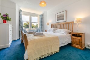 A bedroom with a bed, bedside tables, a window with curtains, a bedside lamp, and a framed picture on the wall. - 5 Bed in Trebetherick (oc-b29371) (La Mohay)