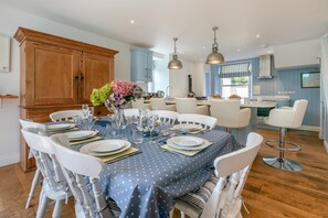 A dining area with a round table set for six, surrounded by white chairs. - 5 Bed in Trebetherick (oc-b29371) (La Mohay)