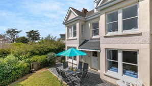 A two-story house with a patio area featuring a table and chairs, a blue umbrella, and a small white table. - 5 Bed in Trebetherick (oc-b29371) (La Mohay)