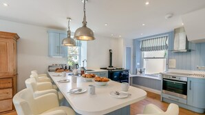 A modern kitchen with a central island, white chairs, and a built-in oven. - 5 Bed in Trebetherick (oc-b29371) (La Mohay)