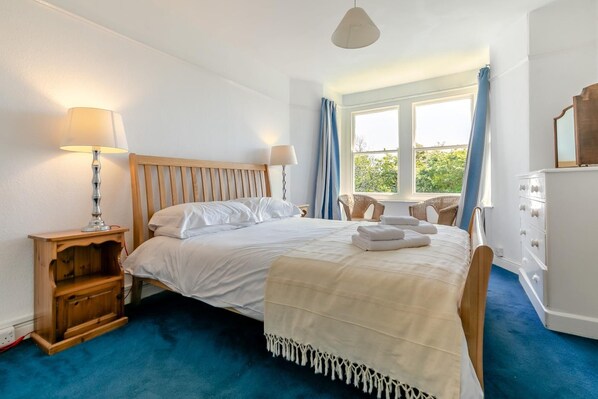 A bedroom with a bed, bedside lamps, a dresser, and a window with curtains. - 5 Bed in Trebetherick (oc-b29371) (La Mohay)
