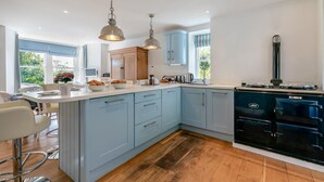 A modern kitchen with light blue cabinets, a black stove, and pendant lights. - 5 Bed in Trebetherick (oc-b29371) (La Mohay)
