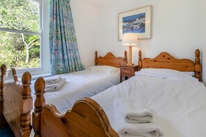 Une chambre d’hôtel avec deux lits en bois, une table de chevet, une lampe, une fenêtre avec des rideaux et un tableau encadré au mur.