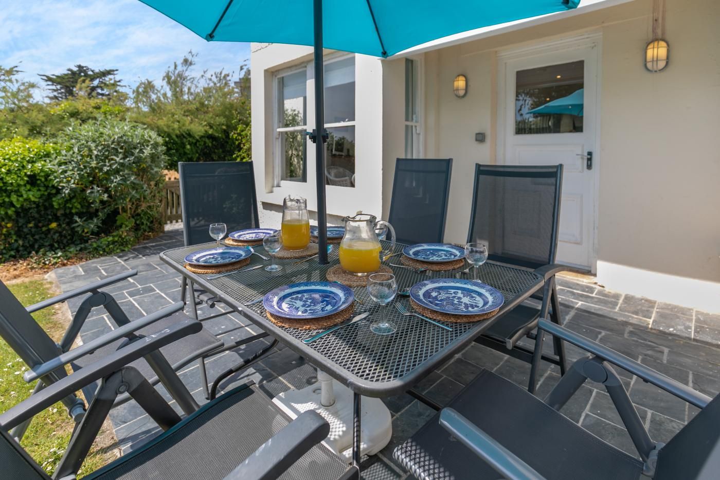 An outdoor dining area with a table set for two, featuring blue and white plates, glasses, and a pitcher of orange juice.