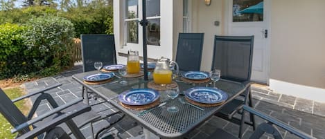 An outdoor dining area with a table set for two, featuring blue and white plates, glasses, and a pitcher of orange juice.