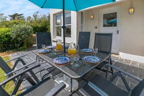 An outdoor dining area with a table set for two, featuring blue and white plates, glasses, and a pitcher of orange juice. - 5 Bed in Trebetherick (oc-b29371) (La Mohay)