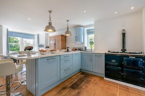 A modern kitchen with light blue cabinets, a black stove, and pendant lighting. - 5 Bed in Trebetherick (oc-b29371) (La Mohay)
