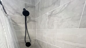 A shower with a handheld showerhead, tiled walls, and a drain. - Charming 1-bedroom in-law suite with functional kitchen in pleasant Portsmouth (Portsmouth)