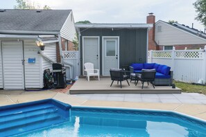 Un patio trasero con piscina, un patio con mobiliario exterior y un garaje.