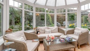 Ein Wintergarten mit Korbmöbeln, einem Glastisch und Blick auf den Garten.