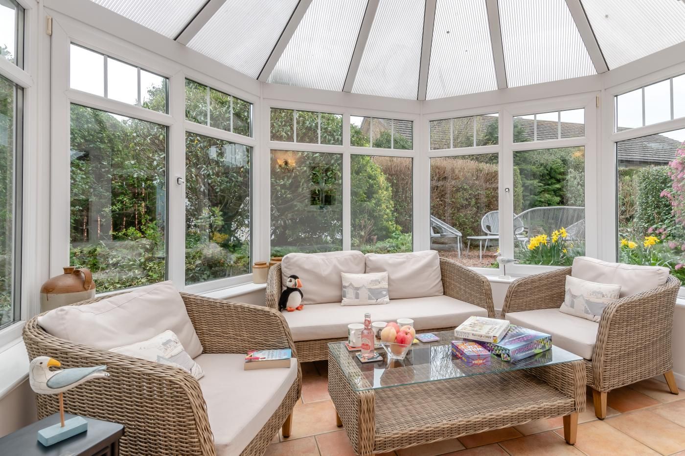 A conservatory with wicker furniture, a glass table, and a view of the garden.