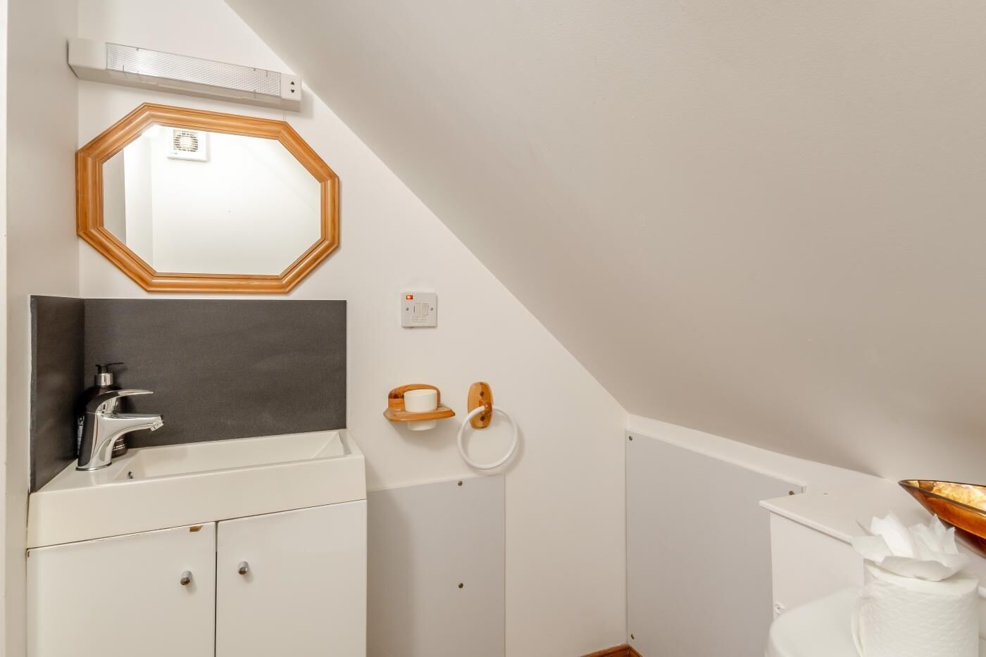 Ein Badezimmer mit einem weißen Waschbecken, einem Spiegel mit Holzrahmen, einem Handtuchhalter und einer Toilette mit Papierhandtuchspender.