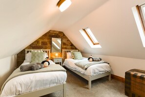 Une chambre mansardée chaleureuse avec deux lits, un mur en pierre, une lucarne et une petite commode en bois.