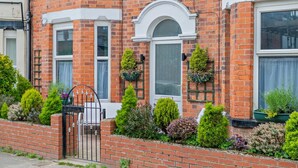 A brick house with a white door, a small window, and a white-framed window. There are green plants in pots on the wall. - 6 Bed in Bridlington (oc-n29516) (Bridlington)