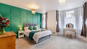 A bedroom with a large bed, a bedside table, a dresser, a vanity, and a window with curtains. - 6 Bed in Bridlington (oc-n29516) (Bridlington)