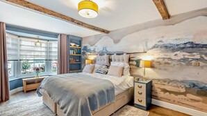 A bedroom with a bed, bedside tables, a window with curtains, a bookshelf, and a wall mural.
