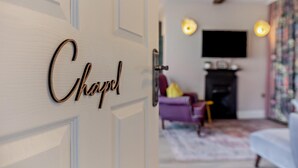 A room with a door labeled 'Chapel,' a fireplace, a television, and a purple armchair.