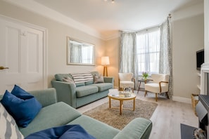 A living room with a sofa, armchairs, a coffee table, a lamp, a TV, and a window with curtains. - 2 Bed in Padstow (oc-lnews) (Padstow)