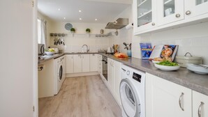 Een compacte keuken met witte kastjes, een wasmachine en een eethoek met een boek en borden.