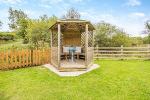A wooden gazebo with a table and chairs, surrounded by a wooden fence and lush greenery. - 2 Bed in Devils Bridge (oc-d29575) (Pontarfynach)