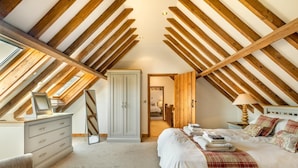 Een zolderkamer met zichtbare houten balken, een kledingkast, een bed met een geruite plaid en een nachtkastje met een lamp.