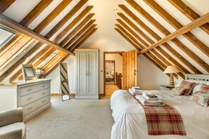 Un dormitorio en el ático con vigas de madera a la vista, un armario, una cama con manta escocesa y una mesita de noche con lámpara.