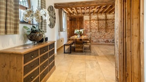 Een rustiek interieur met blootgelegde bakstenen muren, houten balken, een houten eettafel en een grote klok aan de muur.
