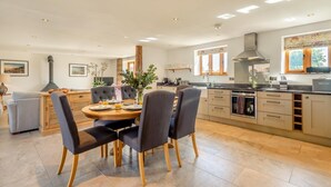 A modern kitchen with a dining area, featuring a central island, wooden cabinets, and a large window. - 3 Bed in Lower Bodham (oc-p29593) (Bodham)