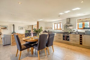 A modern kitchen with a dining area, featuring a central island, wooden cabinets, and a large window. - 3 Bed in Lower Bodham (oc-p29593) (Bodham)