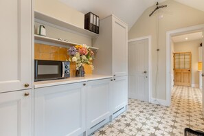 A kitchen with white cabinets, a microwave, and a vase with flowers on the counter. - 2 Bed in Wells-next-the-Sea (oc-c29565) (Wells-next-the-Sea)