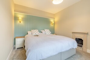 A bedroom with a bed, bedside tables, a nightstand, a fireplace, and wall-mounted lamps. - 2 Bed in Wells-next-the-Sea (oc-c29565) (Wells-next-the-Sea)